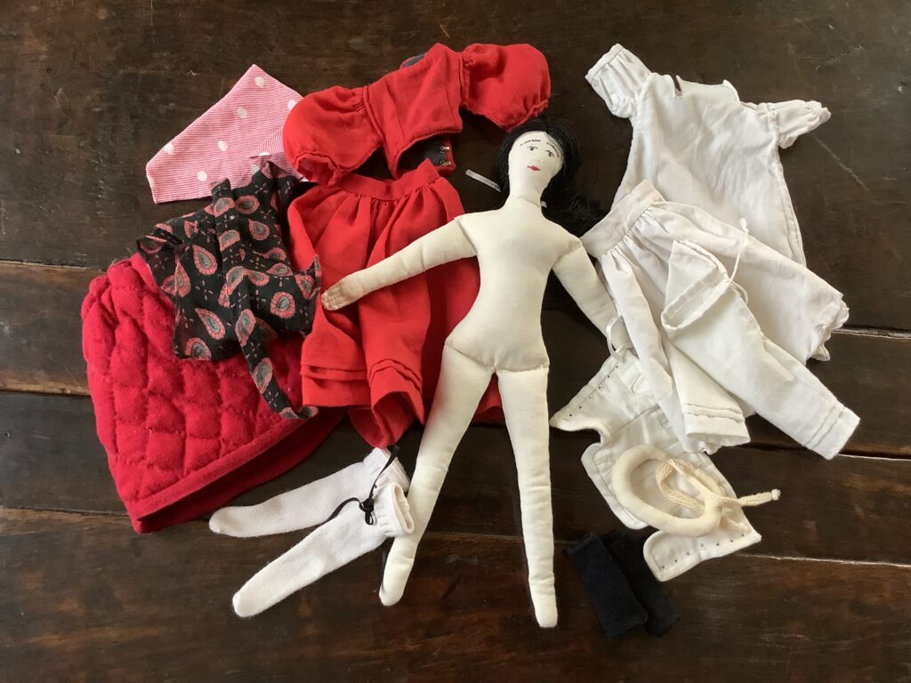 A textile doll surrounded by historical-style clothing